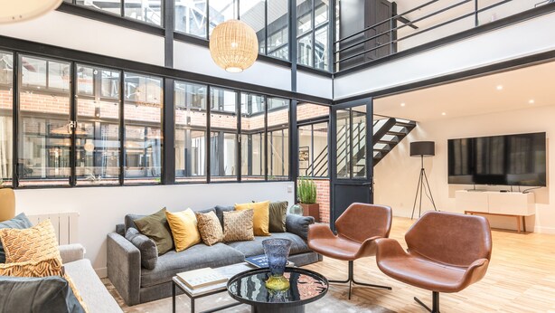 A spacious living area with a grey sofa, brown leather chairs, a coffee table, and large windows offering views of the city. - Hedonist House - Fantastic Architect Loft for 10 guests near Metro (Paris)