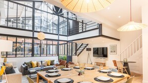 A spacious, modern dining area with a high ceiling, large windows, and a staircase leading to an upper level. - Hedonist House - Fantastic Architect Loft for 10 guests near Metro (Paris)