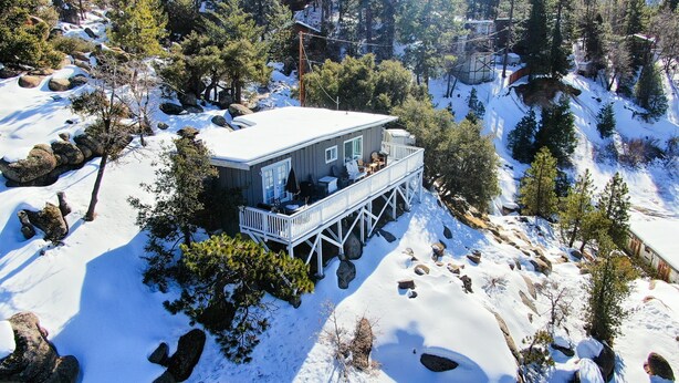 Une cabane dotée d’une terrasse, entourée de neige et d’arbres.