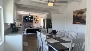 Une cuisine moderne avec un coin repas, comprenant un îlot central, des meubles blancs et un ventilateur de plafond.