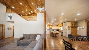 A modern interior with a wooden ceiling, a dining area with a wooden table and chairs, and a kitchen with wooden cabinets. - Ultimate Mtn Retreat - W/ Game room|Fire Pits|Views| 2 Bunk Rooms & Much More! (Duck Creek Village)