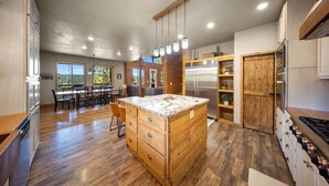 A spacious kitchen with wooden cabinetry, a central island, and a dining area with a view. - Ultimate Mtn Retreat - W/ Game room|Fire Pits|Views| 2 Bunk Rooms & Much More! (Duck Creek Village)