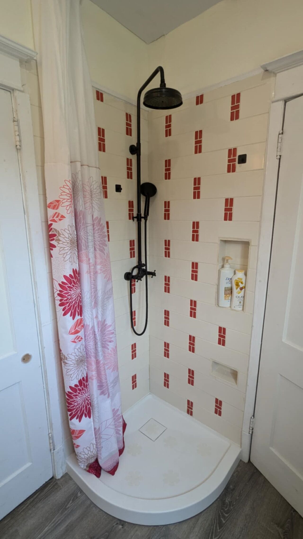 Ein Duschbereich mit weiß gefliester Wand, einer Duschbrause und einer kleinen Ablage für Pflegeprodukte.