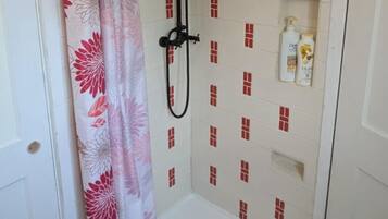Ein Duschbereich mit weiß gefliester Wand, einer Duschbrause und einer kleinen Ablage für Pflegeprodukte.
