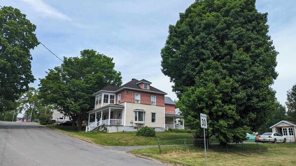 Une maison à deux étages avec un porche et un grand arbre devant.