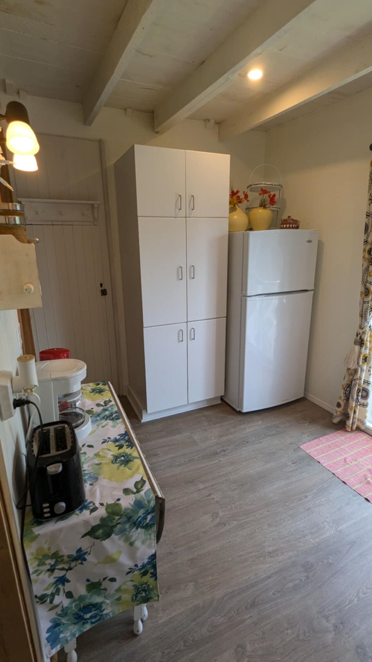 Una cocina pequeña con un refrigerador blanco, un armario de madera y un mantel estampado con motivos florales.