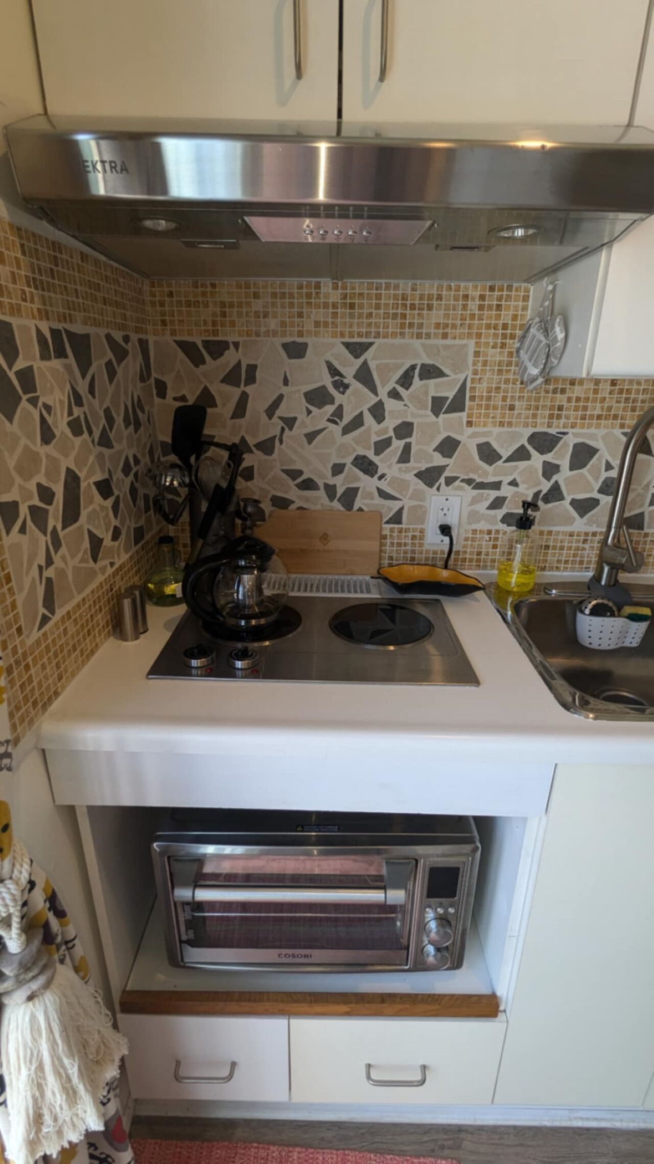 A compact kitchen with a built-in stove, a toaster oven, and a backsplash of mosaic tiles.