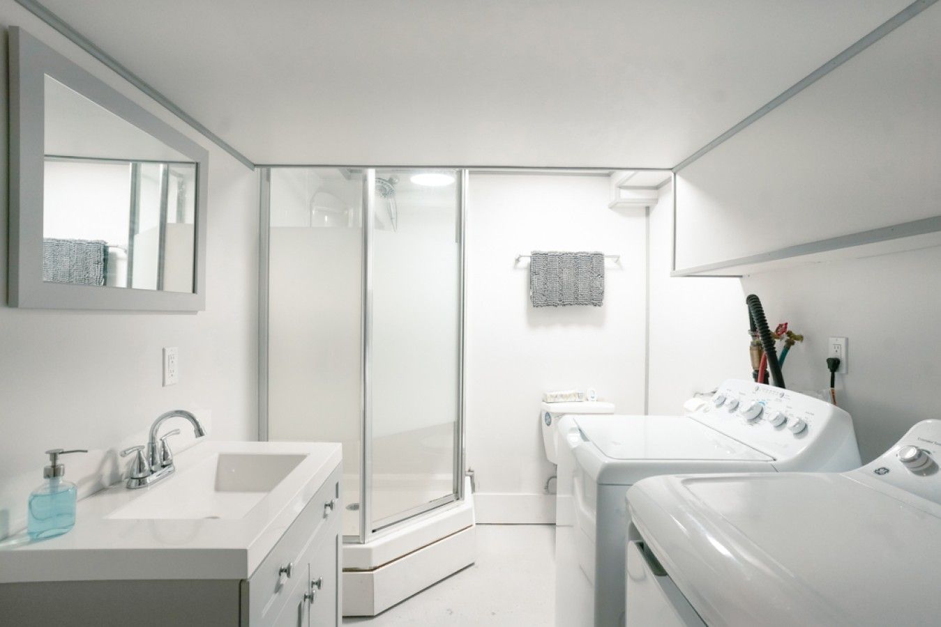 Een moderne badkamer met een douchecabine van glas, een wit wastafelmeubel met spiegel en een witte wasmachine.