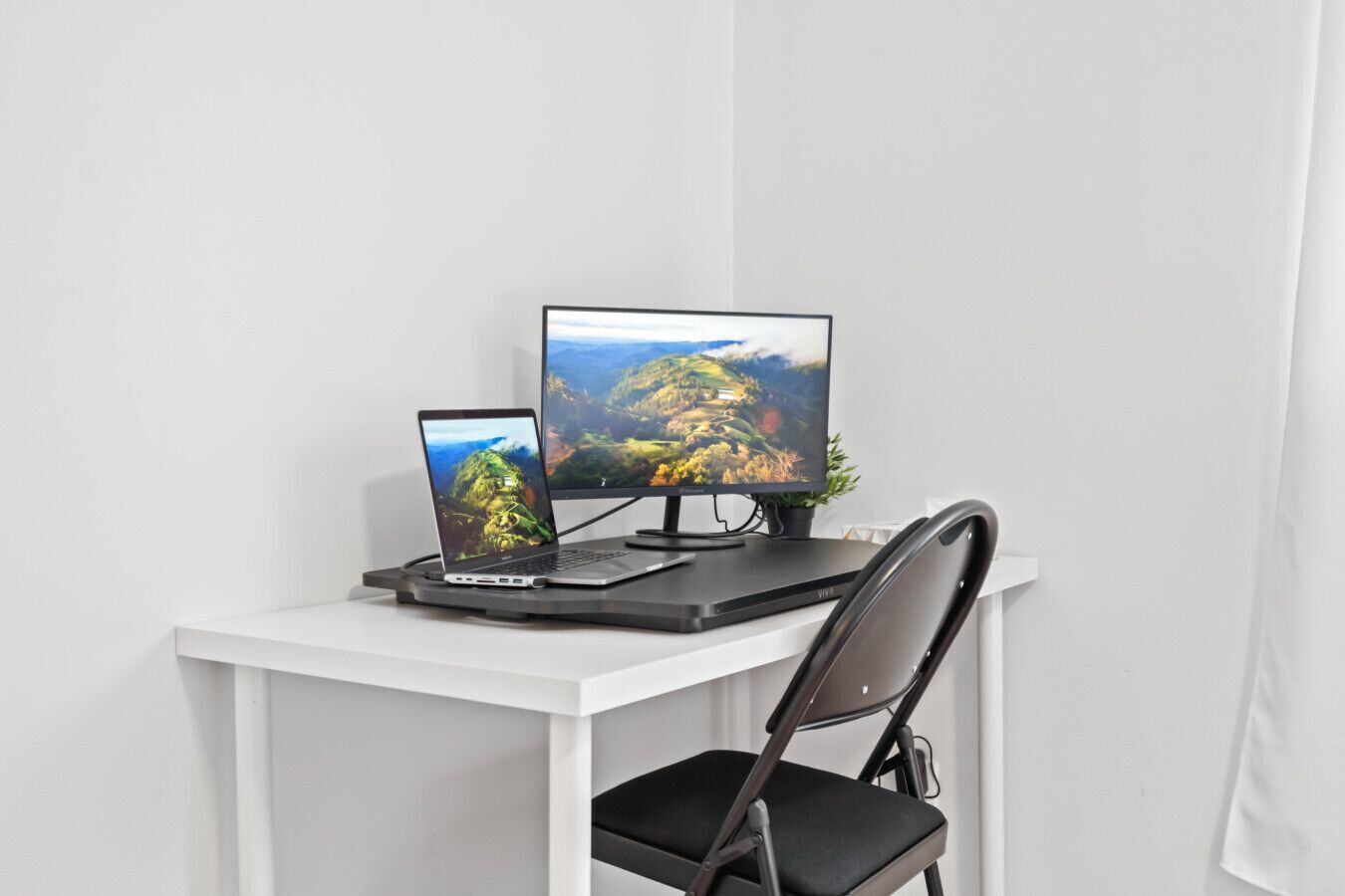 Un escritorio blanco con una computadora portátil y dos monitores, una silla negra y una planta pequeña.