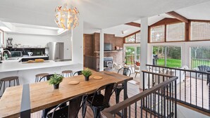 Una cocina moderna con una isla central, un comedor con mesa y sillas de madera, y vistas al exterior a través de amplios ventanales.