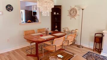 Un coin repas avec une table en bois, des chaises en osier, un lustre, une horloge et une bibliothèque.
