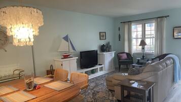 Un salon comprenant une table à manger en bois, un canapé, un téléviseur et un lustre.