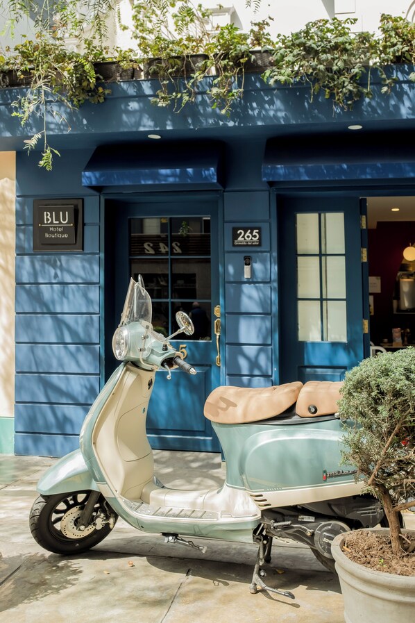 Una scooter antigua estacionada frente a un edificio azul con un letrero que dice 'BLU Hotel Boutique' y el número '265'.