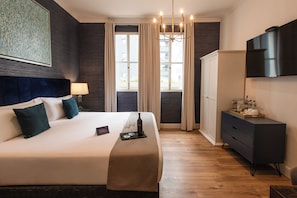 Quarto de hotel com uma cama grande, mesa de cabeceira com abajur, guarda-roupa, televisão e janela com cortinas.
