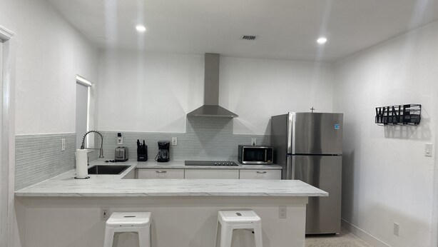 A modern kitchen with white countertops, stainless steel appliances, and a central island with stools. - Beach Apartment in Hollywood  (Hollywood)
