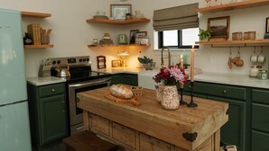 A kitchen with green cabinets, a wooden island, a refrigerator, and various kitchen items.