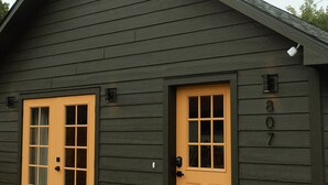 A two-story building with a dark exterior and two doors, one with a window and the other with a mailbox.