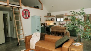 A cozy living room with a brown leather couch, a wooden ladder, a light blue refrigerator, a wooden dining table, and a green plant.