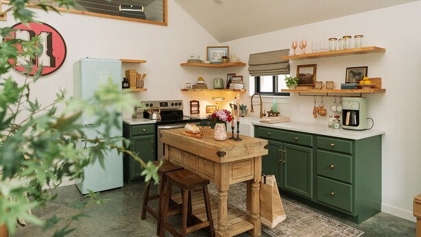 A compact kitchen with green cabinets, a wooden island, and a refrigerator.