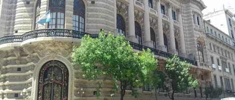Un edificio histórico con arquitectura ornamentada, una entrada imponente y una calle bordeada de árboles.