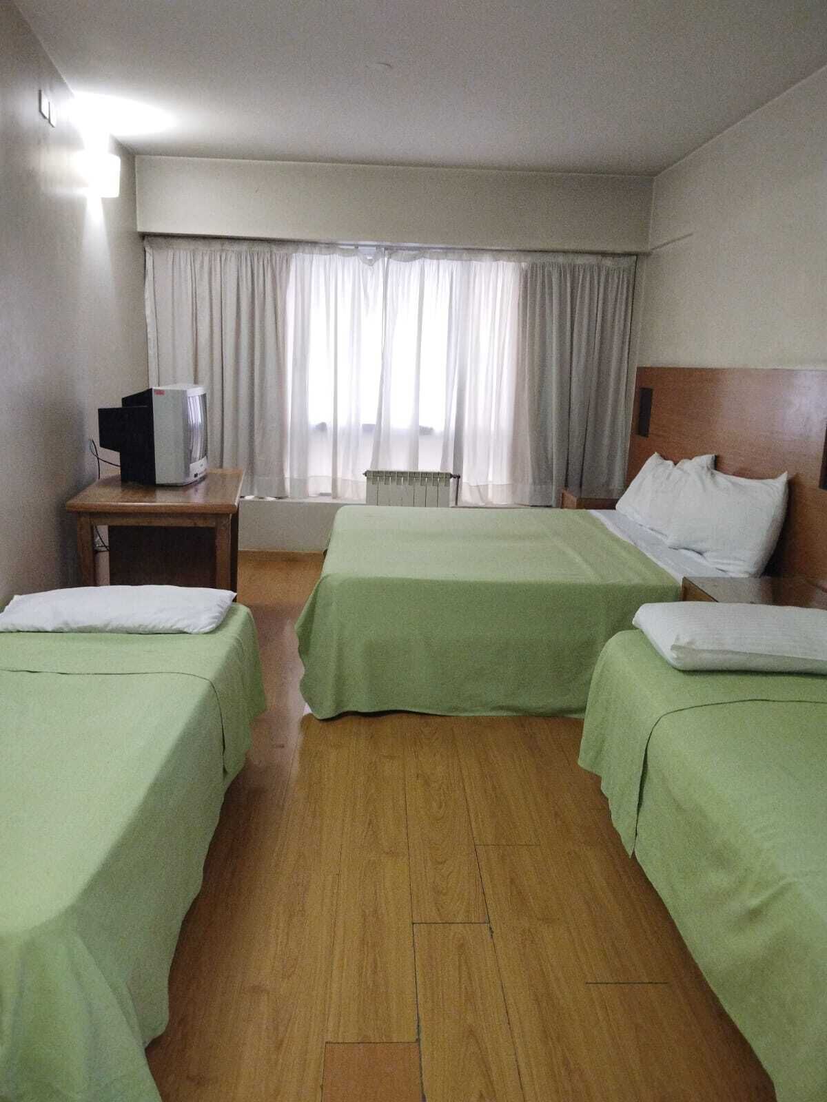 Habitación de hotel con dos camas, piso de madera, escritorio con televisor y ventana con cortinas.