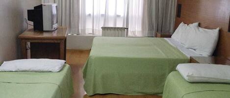 A hotel room with two beds, a wooden floor, a desk with a television, and a window with curtains.