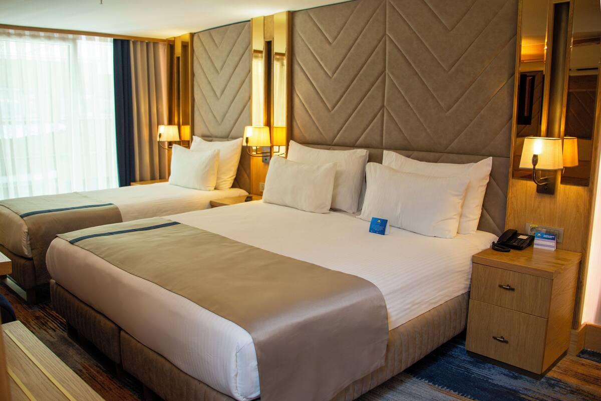 Une chambre d’hôtel avec deux lits, une table de chevet, un miroir et une lampe.