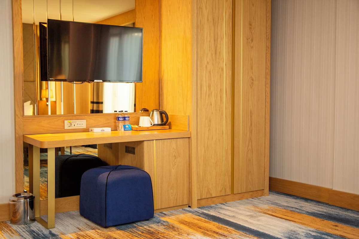 Une chambre d’hôtel compacte comprenant un bureau en bois, un téléviseur à écran plat, un petit coin salon et une poubelle.