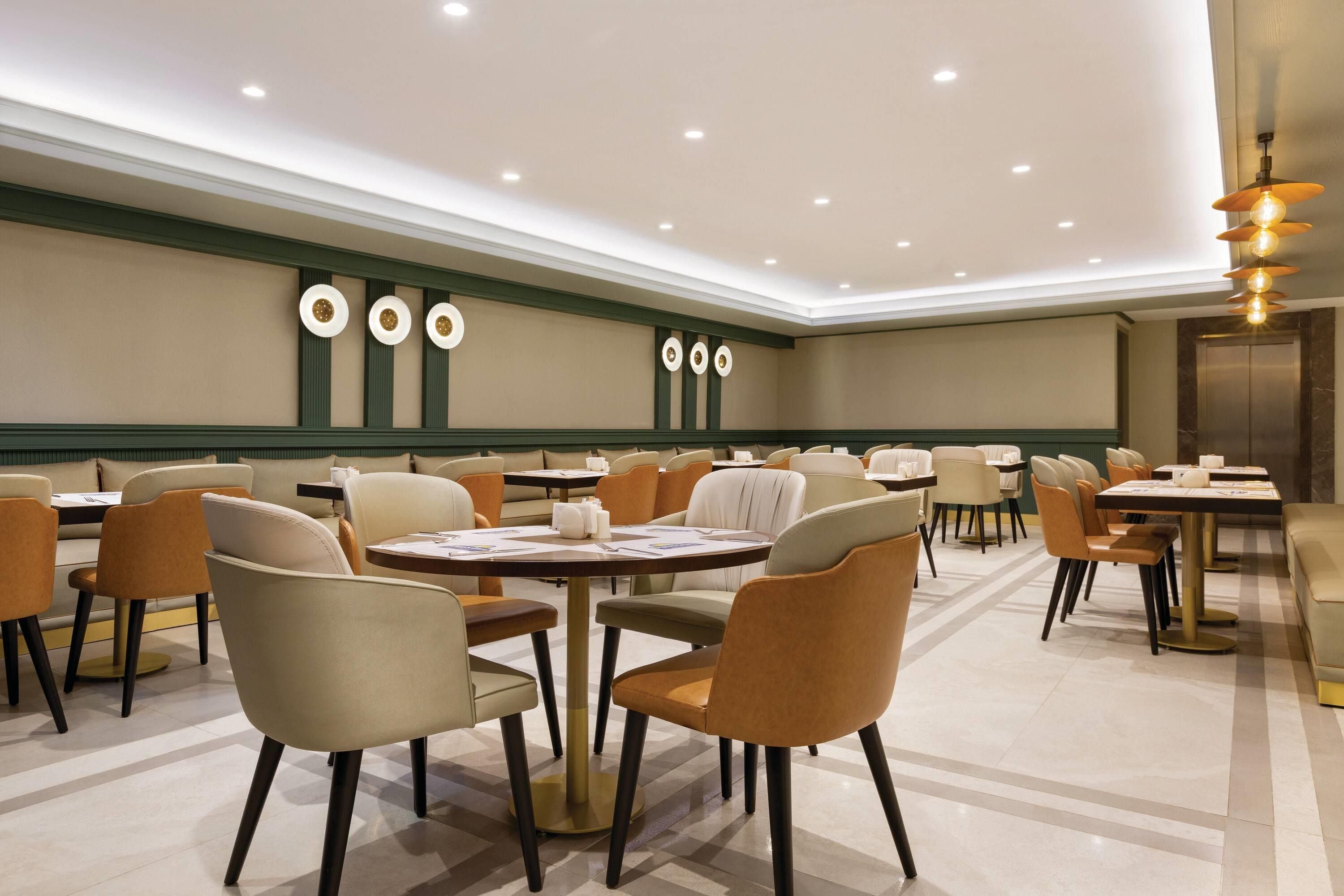 A hotel dining area with round tables and chairs, a ceiling with recessed lighting, and a wall with circular decorative elements.