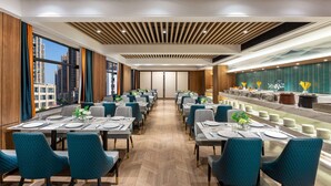 A modern dining area with long tables and teal chairs, a wooden ceiling, and a city view.