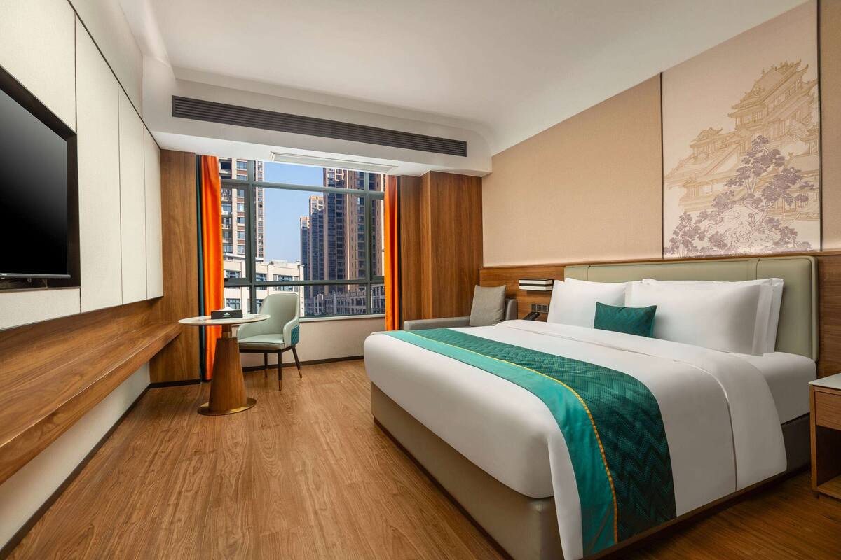 Habitación de hotel con una cama grande, un escritorio, una silla, un televisor y una ventana con vistas a la ciudad.