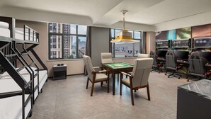 A modern room with a bunk bed, a gaming table, gaming chairs, and a large window with a city view.