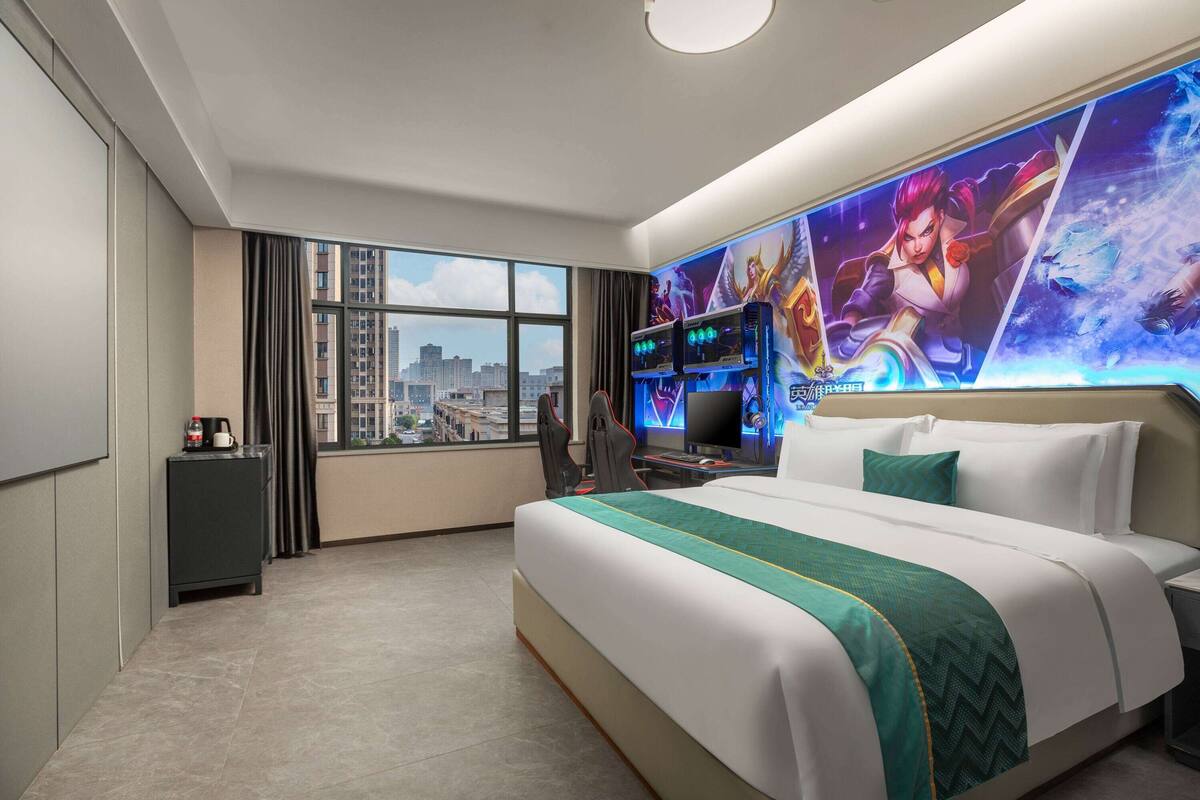 Una habitación de hotel con una cama grande, un escritorio con una computadora, una silla, un televisor y vistas a la ciudad desde la ventana.
