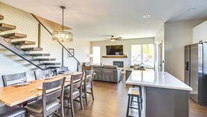 A modern kitchen with a central island, a dining area with wooden chairs and a table, and a staircase with a light fixture. - Ski-In/Ski-Out Granby Townhouse w/ Private Hot Tub (Granby)