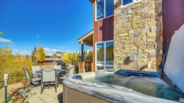 A hot tub in a backyard with a stone wall and a wooden deck. - Ski-In/Ski-Out Granby Townhouse w/ Private Hot Tub (Granby)