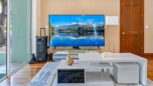 A modern living room with a large flat-screen TV, a white coffee table, and a wooden door. - Lakeview Chic 3BD House for golf/beach lovers (Clearwater)