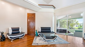 A spacious living room with hardwood flooring, two modern sofas, a glass coffee table, and a large sliding glass door leading to an outdoor area. - Lakeview Chic 3BD House for golf/beach lovers (Clearwater)