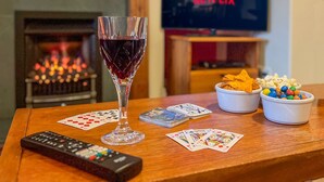 Un saló amb una llar de foc, un got de vi negre, cartes, un comandament a distància i plats d'aperitius.