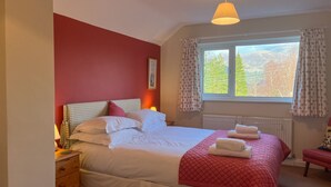 Un llit ben arriscat amb roba de llit blanca, una paret vermella d'accent, una finestra amb cortines, un radiador i una làmpada de nit.
