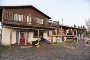 A two-story wooden building with a balcony, a red door, and a covered outdoor area with steps leading to a higher level. - The McCall House- Hot Tub, A/C, Huge Covered Patio (McCall)
