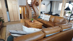 Un vaste salon doté d’un canapé en cuir marron, d’une table basse en bois et d’un escalier menant à un niveau supérieur.