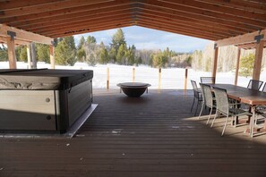 A covered outdoor deck with a hot tub, a table with chairs, and a view of a snowy landscape. - The McCall House- Hot Tub, A/C, Huge Covered Patio (McCall)