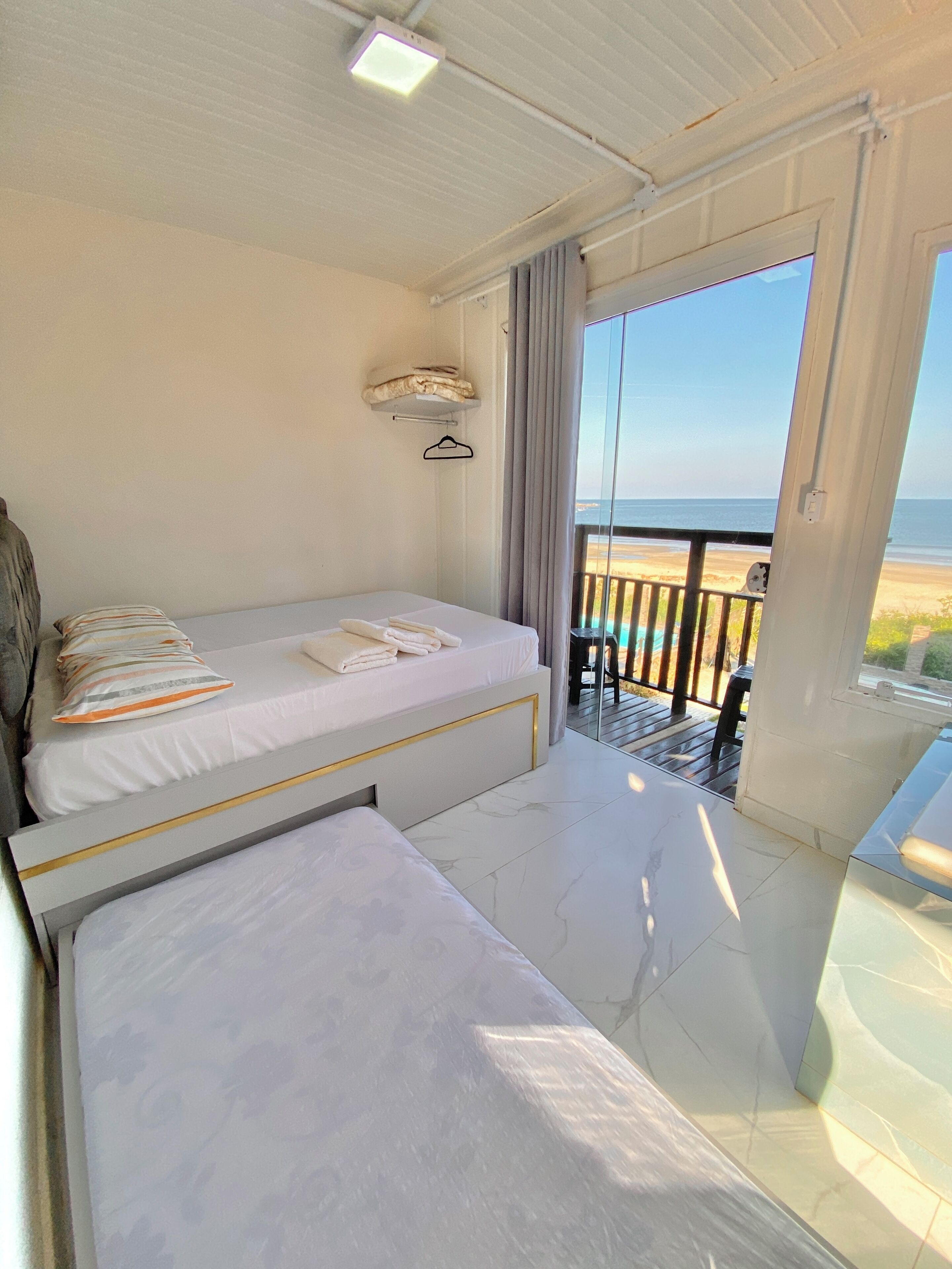 A room with a bed, a bench, a small table, and a view of the beach.
