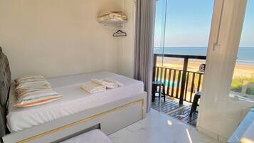 A room with a bed, a bench, a small table, and a view of the beach.