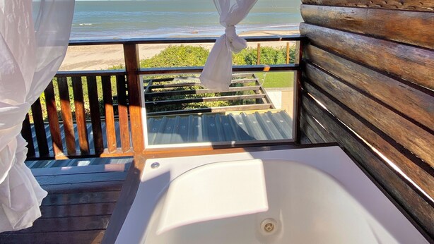A balcony with a view of the sea, a wooden cabin structure, and a white bathtub. - POUSADA SAO MIGUEL BEACH (Penha)