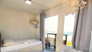 A bedroom with a bed, a glass-enclosed bathroom, and a balcony with a view of the beach. - POUSADA SAO MIGUEL BEACH (Penha)