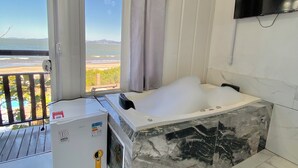 A modern bathroom with a large bathtub, a refrigerator, and a television on the wall. - POUSADA SAO MIGUEL BEACH (Penha)