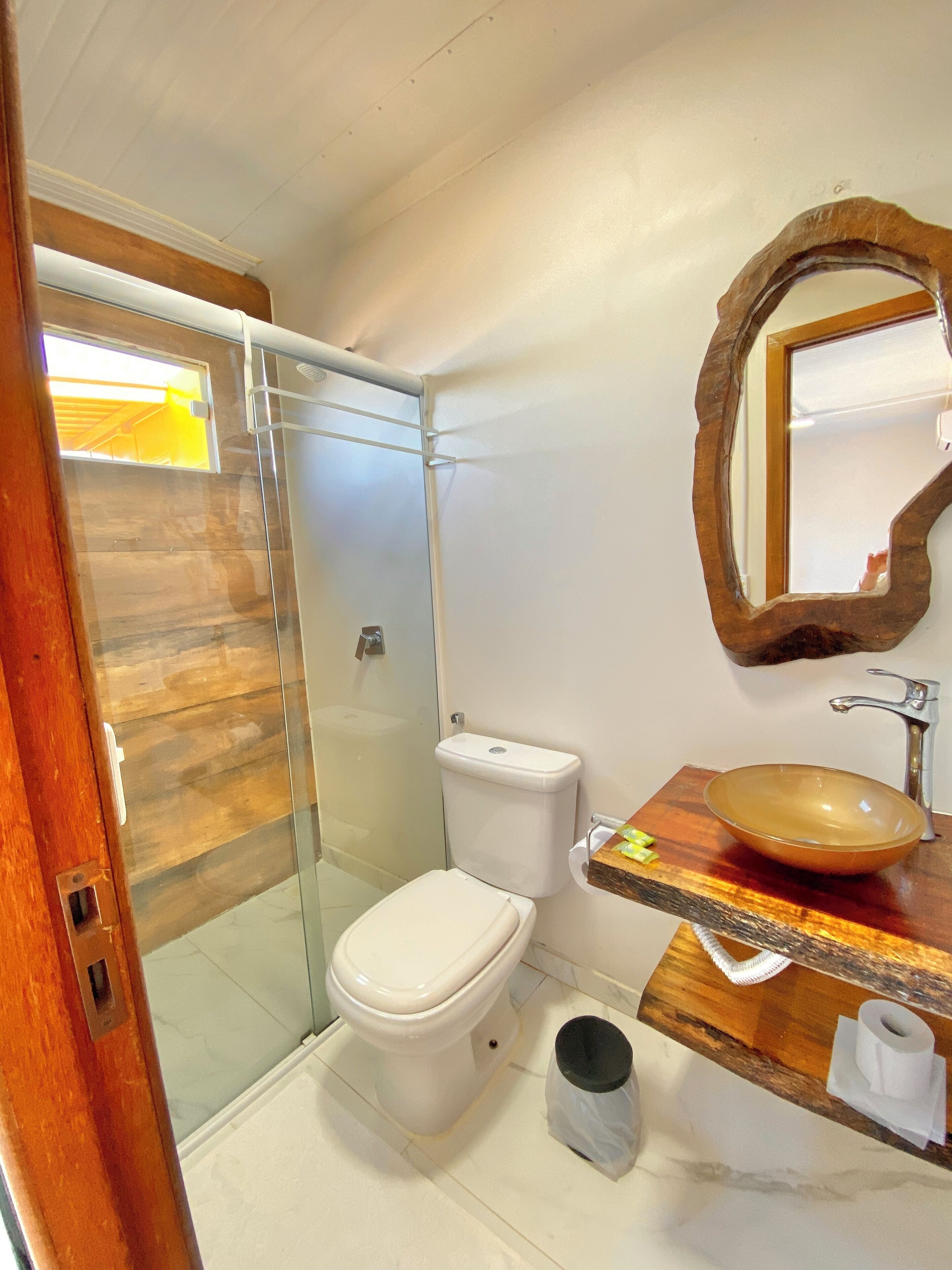 Ein Badezimmer mit einer gläsernen Duschkabine, einer weißen Toilette und einem hölzernen Waschtisch mit rundem Waschbecken.