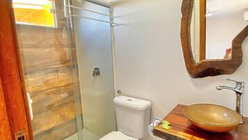 Ein Badezimmer mit einer gläsernen Duschkabine, einer weißen Toilette und einem hölzernen Waschtisch mit rundem Waschbecken.