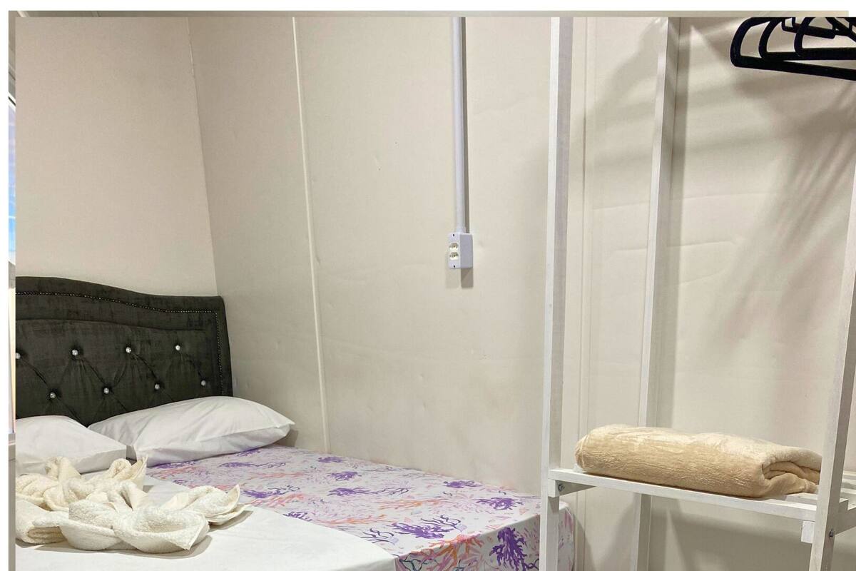 A hotel room with a bed, a white shelf unit, and a red bed base.